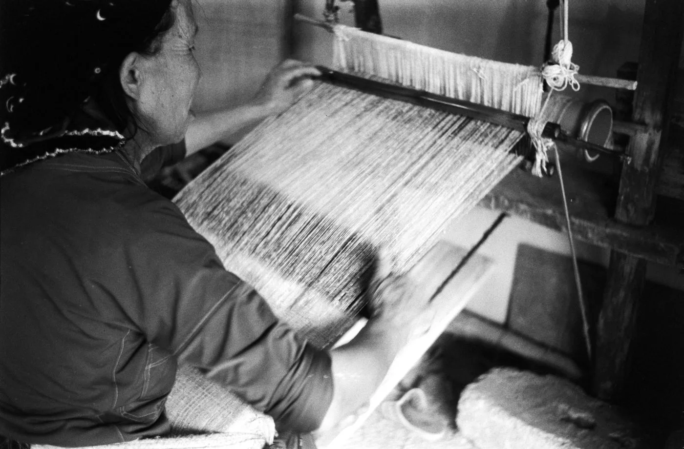 Black and white photograph of a woman working at a traditional loom