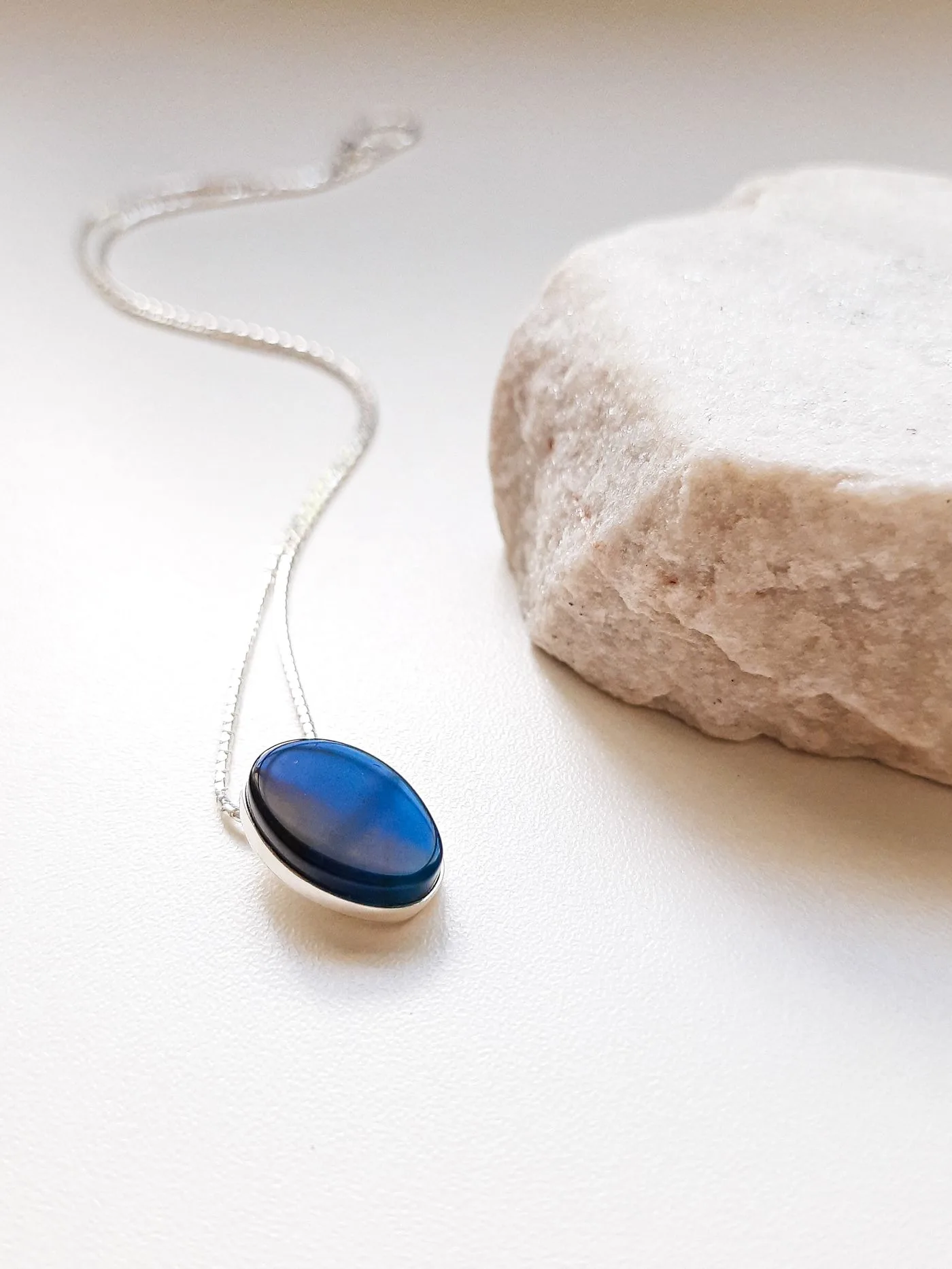 A blue stone pendant on a silver-colored chain beside pale textured stone