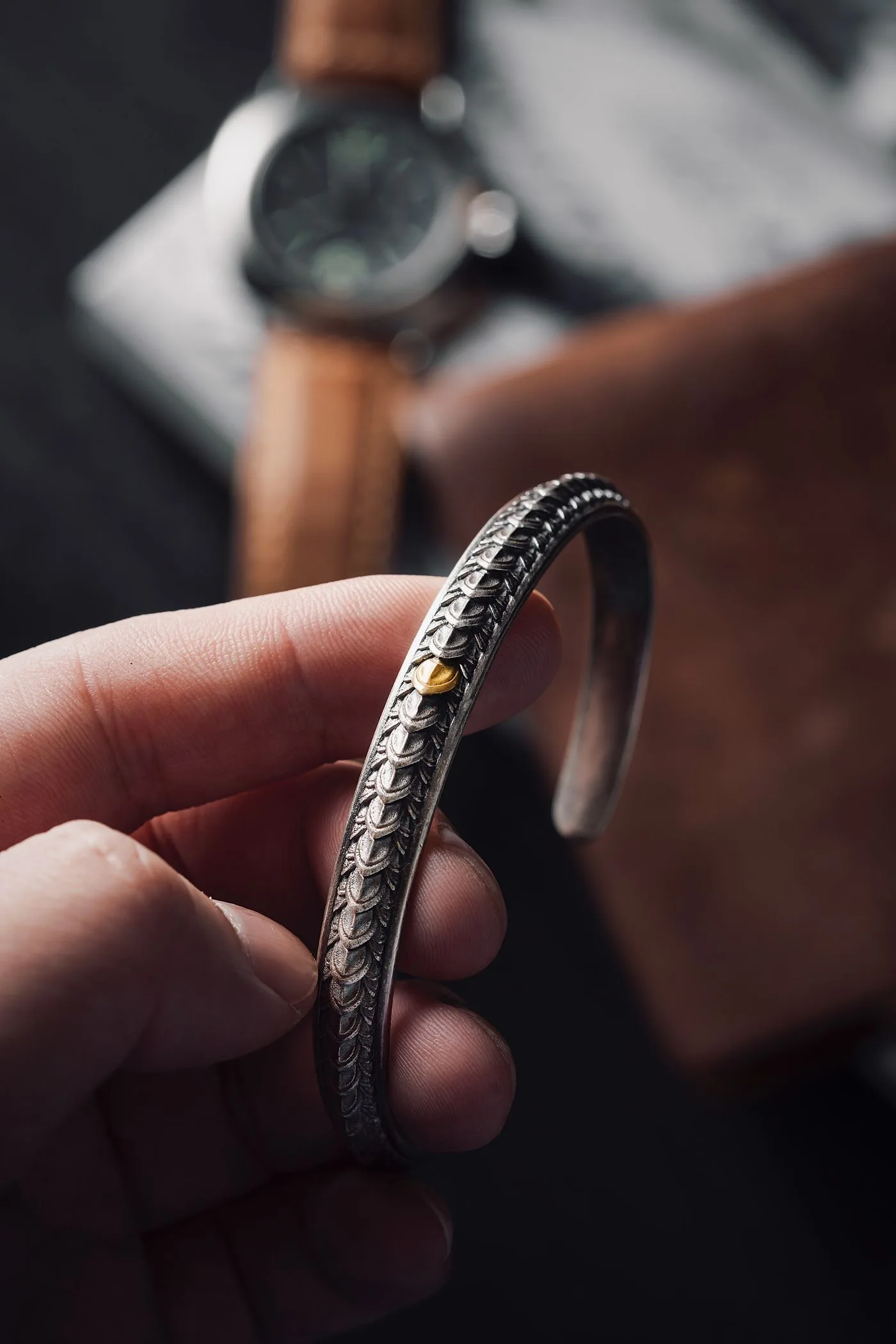 A hand holding an intricately patterned silver-colored cuff