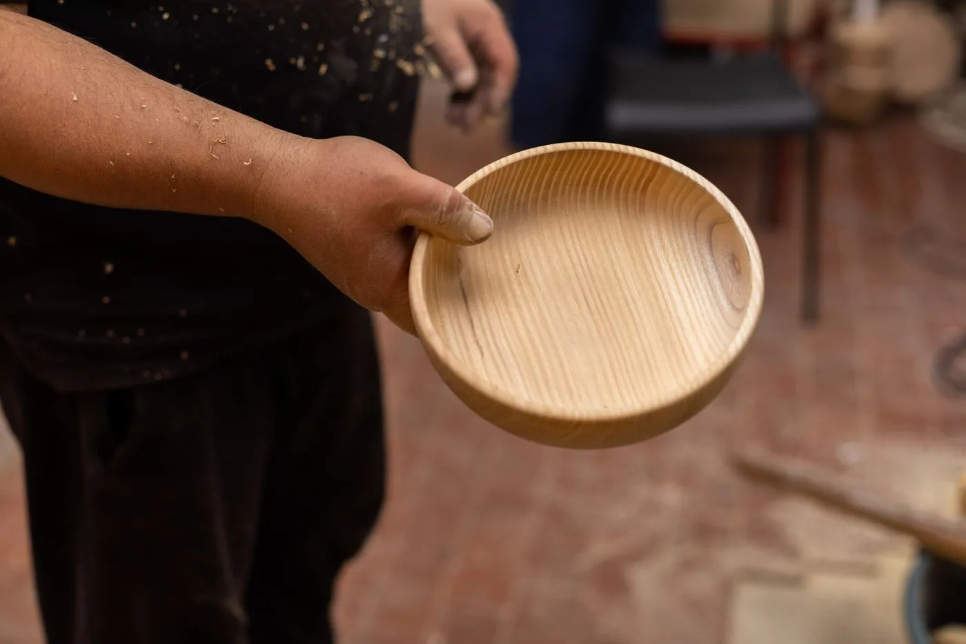 A woodworker holding a freshly turned wooden bowl in a workshop